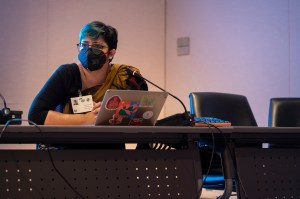 Srinidhi is dressed in a saree and seated in front of her computer. She is wearing a mask.