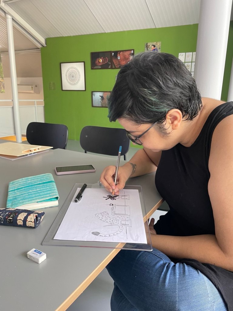 Srinidhi dressed in a black top and jeans drawing something on a desk.